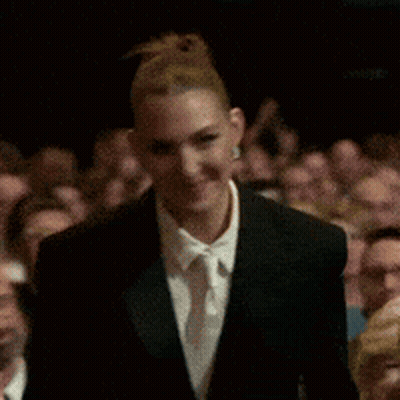 A Woman In A Suit And Tie Is Clapping In Front Of A Crowd . GIF
