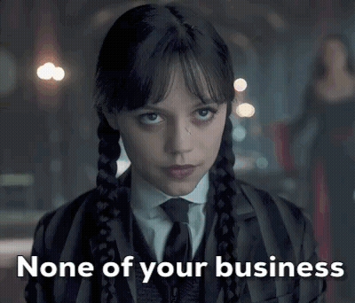 A Woman In A Suit And Tie Is Looking At The Camera With The Words `` None Of Your Business '' Written Below Her . GIF