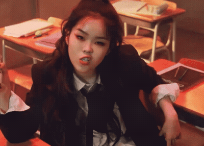 A Woman In A Suit And Tie Is Sitting At A Desk GIF
