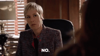 A Woman In A Suit And Tie Is Sitting In A Chair And Says No . GIF