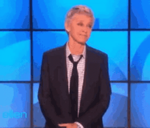 A Woman In A Suit And Tie Is Standing In Front Of A Blue Screen With The Word Ellen On It GIF