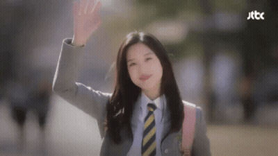 A Woman In A Suit And Tie Is Waving Her Hand . GIF