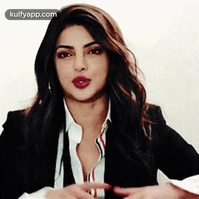 A Woman In A Suit And White Shirt Is Making A Gesture With Her Hands . GIF