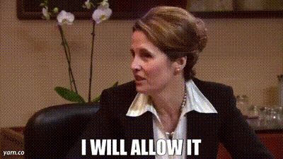 A Woman In A Suit And White Shirt Is Sitting In A Chair And Saying I Will Allow It . GIF