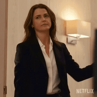 A Woman In A Suit And White Shirt Is Standing In A Room . GIF