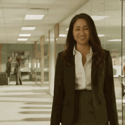 A Woman In A Suit And White Shirt Smiles While Walking Down A Hallway GIF