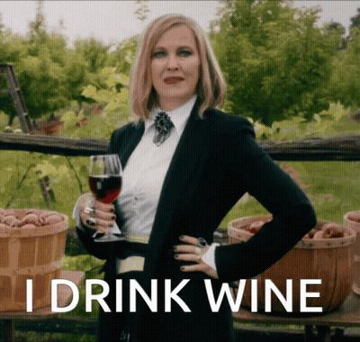 A Woman In A Suit Holding A Glass Of Wine With The Words I Drink Wine Above Her GIF