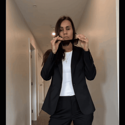 A Woman In A Suit Is Adjusting Her Sunglasses In A Hallway GIF