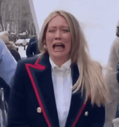 A Woman In A Suit Is Crying While Standing In A Crowd Of People . GIF
