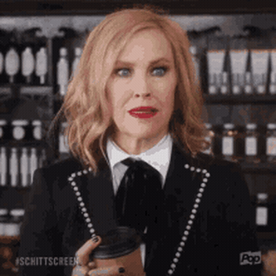 A Woman In A Suit Is Holding A Cup Of Coffee In Her Hand . GIF