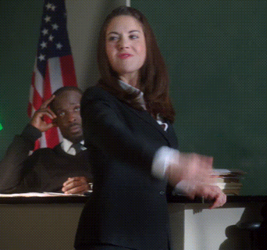 A Woman In A Suit Is Holding Her Fist In The Air And Says Booyah GIF