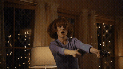 A Woman In A Suit Is Holding Two Guns In Front Of A Table GIF