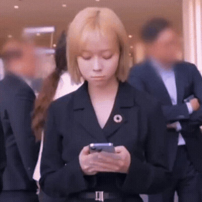A Woman In A Suit Is Looking At Her Cell Phone While Standing In A Crowd Of People . GIF