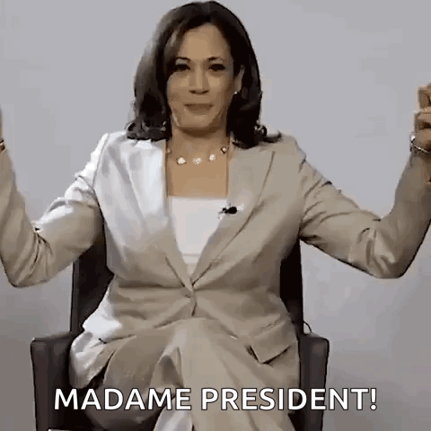 A Woman In A Suit Is Sitting In A Chair With Her Arms Outstretched And Saying `` Madame President '' . GIF