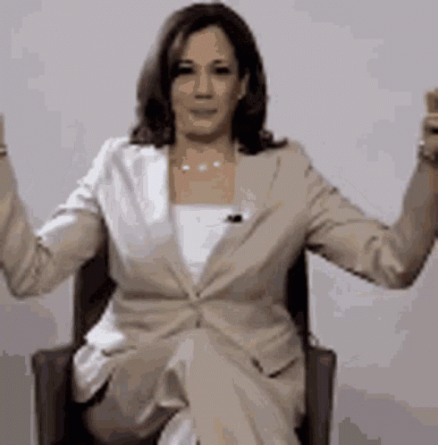 A Woman In A Suit Is Sitting In A Chair With Her Arms Up . GIF