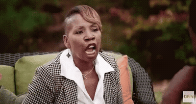 A Woman In A Suit Is Sitting On A Couch Making A Funny Face . GIF