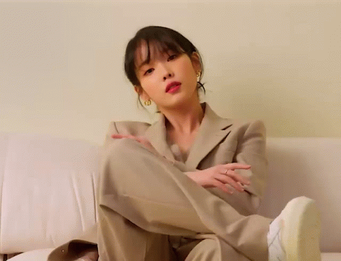 A Woman In A Suit Is Sitting On A Couch With Her Leg Up GIF