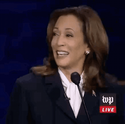 A Woman In A Suit Is Smiling While Speaking Into A Microphone . GIF