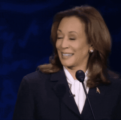 A Woman In A Suit Is Smiling While Standing In Front Of A Microphone GIF