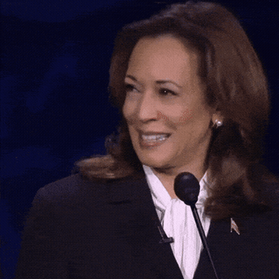 A Woman In A Suit Is Smiling While Standing In Front Of A Microphone GIF
