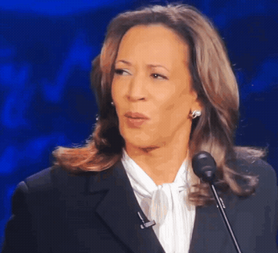 A Woman In A Suit Is Speaking Into A Microphone And Making A Funny Face GIF