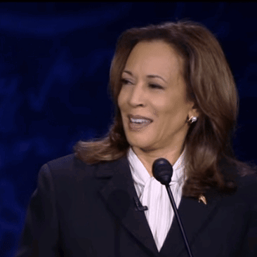 A Woman In A Suit Is Speaking Into A Microphone While Smiling GIF