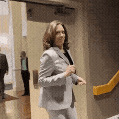 A Woman In A Suit Is Standing In A Hallway . GIF