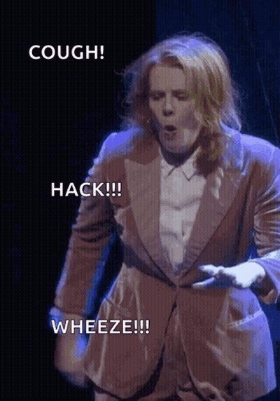 A Woman In A Suit Says Hack Wheeze And Cough On A Stage GIF