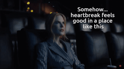 A Woman In A Suit Sits In A Dark Room With The Words " Somehow Heartbreak Feels Good In A Place Like This " Above Her GIF