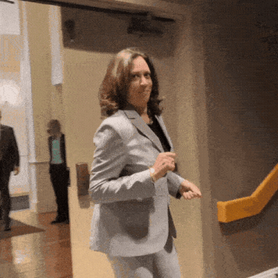 A Woman In A Suit Stands In A Hallway GIF