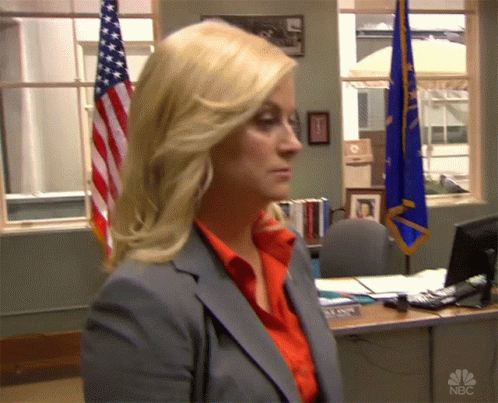 A Woman In A Suit Stands In Front Of A Desk With A Name Tag That Says Mann GIF