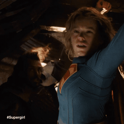 A Woman In A Supergirl Costume Is Holding A Light In Her Hand . GIF