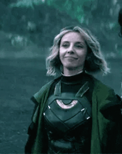 A Woman In A Superhero Costume Is Smiling And Wearing A Green Coat . GIF