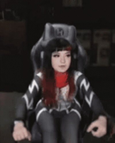 A Woman In A Superhero Costume Is Standing In Front Of A Chair . GIF