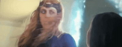 A Woman In A Superhero Costume Is Standing Next To Another Woman In A Room . GIF