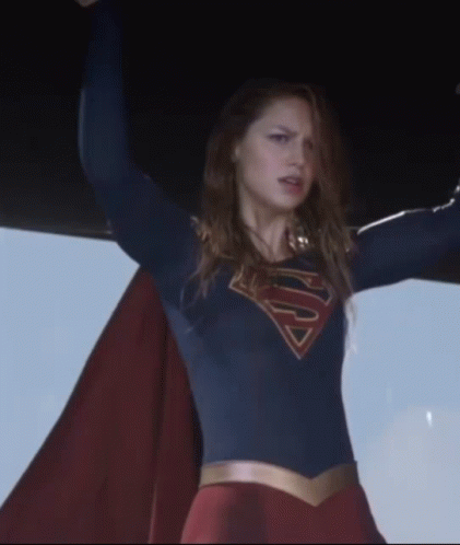 A Woman In A Superman Costume Holds Her Arms Up In The Air GIF