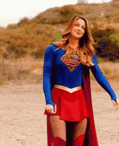 A Woman In A Superman Costume Is Standing In A Dirt Field . GIF