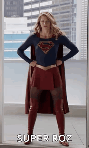 A Woman In A Superman Costume Is Standing In Front Of A Window With Her Hands On Her Hips And Says Super Roz . GIF