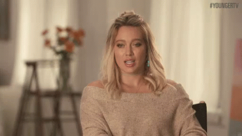 A Woman In A Sweater Is Sitting In A Chair And Making A Face . GIF