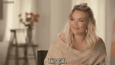 A Woman In A Sweater Is Sitting In A Chair And Smiling While Saying This Girl . GIF