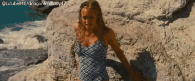 A Woman In A Swimsuit Is Sitting On A Rock Near The Water GIF