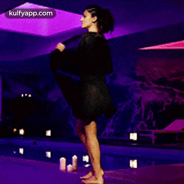 A Woman In A Swimsuit Is Walking On A Runway In Front Of A Swimming Pool . GIF