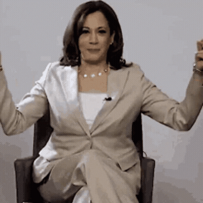 A Woman In A Tan Suit Is Sitting In A Chair With Her Arms Outstretched GIF