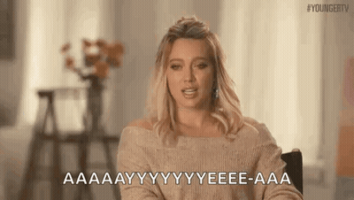 A Woman In A Tan Sweater Is Sitting In A Chair And Talking . GIF