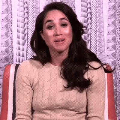 A Woman In A Tan Sweater Is Sitting In Front Of A Patterned Wall GIF