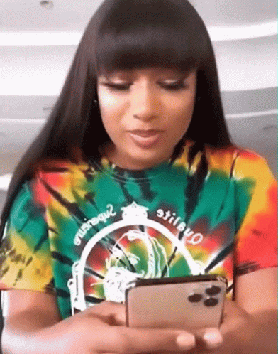 A Woman In A Tie Dye Shirt Is Looking At Her Cell Phone GIF