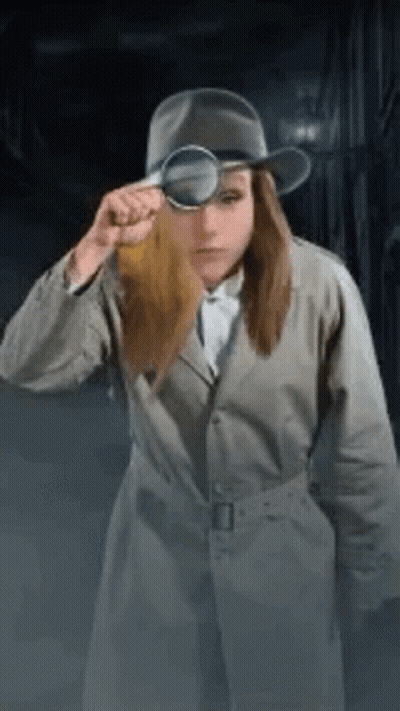 A Woman In A Trench Coat And Hat Is Looking Through A Magnifying Glass . GIF