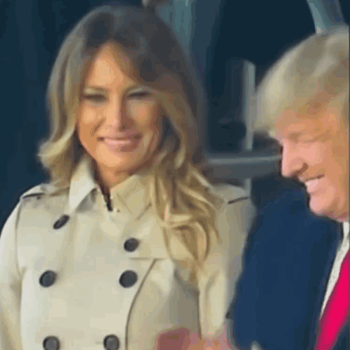 A Woman In A Trench Coat Is Smiling Next To A Man In A Suit . GIF
