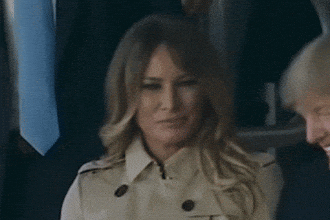 A Woman In A Trench Coat Is Smiling While Sitting Next To A Man In A Suit And Tie . GIF