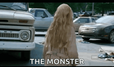 A Woman In A Trench Coat Is Standing In Front Of A Truck And Cars And The Words The Monster Are Written On The Screen . GIF